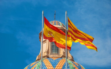 The national flags of Spain and Catalonia are fluttering in the wind against the sky