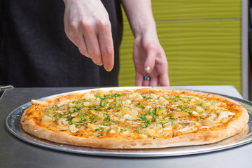 Female hands spread ingredients on pizza
