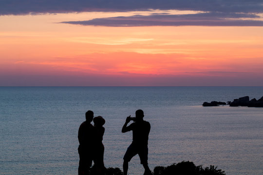 Young couple silhouetted watching a romantic beautiful golden sunset above golden bay, Ghajn Tuffieha, Malta