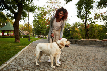 Happy lady hugging her white friendly dog while walking in park