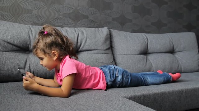 baby girl lying on sofa with tablet. Little girl lying playing on tablet