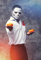 Male african american in the role of a zombie and skeleton. Man is holding two orange pumpkin Halloween holiday symbol. Portrait of an african man - festival, carnival, party, Halloween. Voodoo people