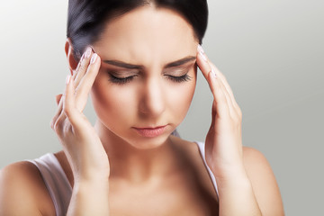 Headache in a beautiful young woman. Fatigue after a working day. Holds a hand in the forehead area. The concept of health. On a gray background.