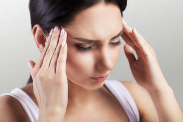 Headache in a young girl. Migraine. Fatigue after a hard working day. The concept of health. On a gray background.