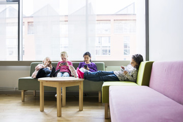 Four girls with feet on table using smartphones