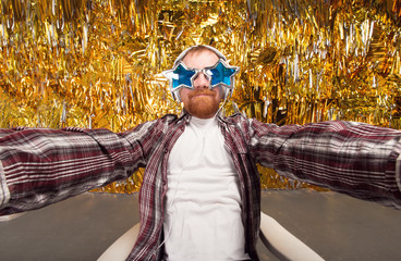 Selfie and party! Happy fun man. Girl with shaped stars glasses. Party club, fun to spend time. Young man holding camera and making selfie and smiling while standing against gold background