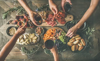 Poster Flat-lay of friends eating and drinking together. Top view of people having party, gathering, celebrating at wooden rustic table set with various wine snacks and fingerfoods. Hands holding glasses © sonyakamoz