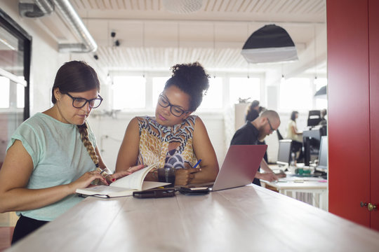 Women working by table at office, coworkers in background