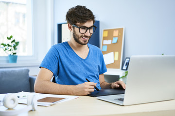 Young graphic designer working on laptop in home office and smiling