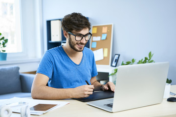 Young graphic designer in home office working on laptop