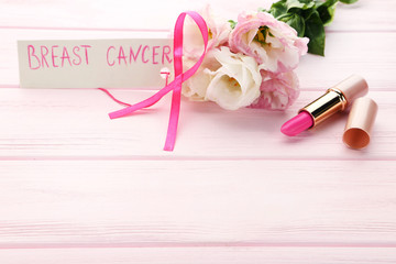 Pink ribbon with flowers, pomade and inscription Breast Cancer on wooden table