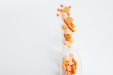 Medical orange pills in glass bottle on white table