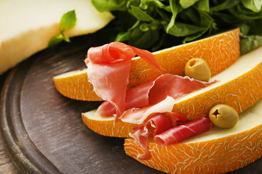 Slices of melon with jamon and olives on cutting board