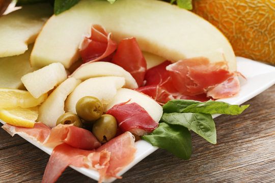 Ripe melons with jamon, olives and basil leafs on wooden table