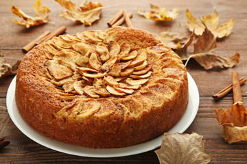 Apple cake in plate with dry leafs on brown wooden table