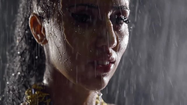 drops of rainfall are dripping on wet face of young pretty woman with hair gathered in the tail