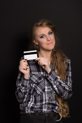 Fototapeta premium Beautiful young caucasian girl in plaid shirt and with long fair-haired hair holds a credit card smiling