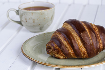 Fresh chocolate croissants and tea cup for breakfast on white wooden vintage table