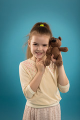 Portrait of a caucasian girl in a studio on a blue isolated background, a baby with a teddy bear in her hands