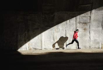 Powerful athlete sprinting and running. Man training and casting shadow in a wall.