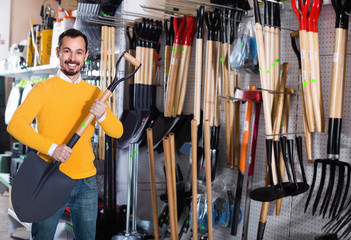 Man choosing new shovel in garden equipment shop