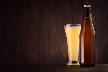 Brown beer bottle NRW and glass pilsner with muddy weizen on dark wood board, copy space, mock up. Template for advertising, design, branding identity.