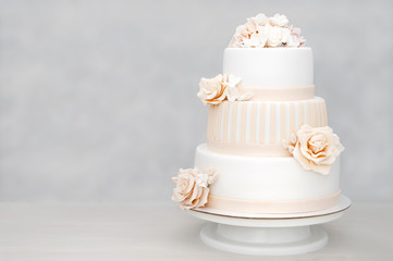 Three-tiered white wedding cake decorated with flowers from mastic on a white wooden table. Picture...