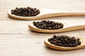 Black pepper in wooden spoon on the old board