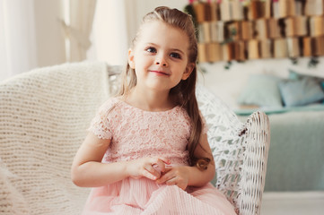portrait of cute smiling 5 years old child girl sitting on chair at home