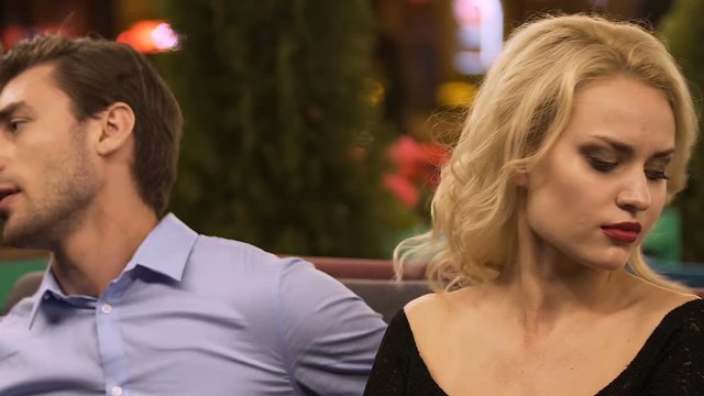 Couple sitting in restaurant, guy touching shoulder of angry girl, apologies