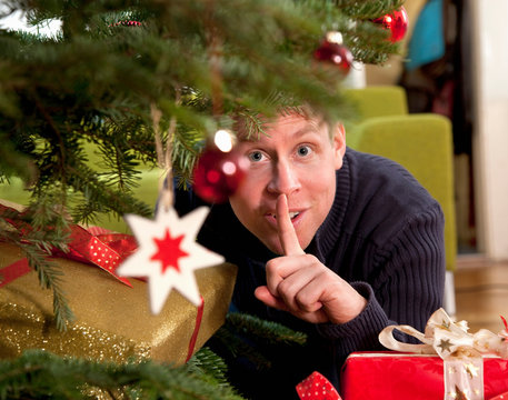 Man Hiding Presents Under Christmas Tree