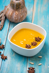 Pumpkin and carrot soup with cream and parsley on blue  wooden background.