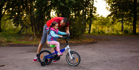 Family sport father and daughter riding bikes in green forest