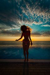 Summer Vacation. Silhouette of beauty dancing woman on sunset near the pool with ocean view.