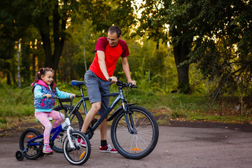 Family sport father and daughter riding bikes in green forest