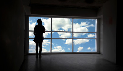 Fototapeta na wymiar Back or rare view of women silhouette beside the big window and sky with cloud background,freedom concept