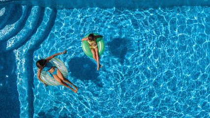 Aerial top view of children in swimming pool from above, happy kids swim on inflatable ring donuts and have fun in water on family vacation
