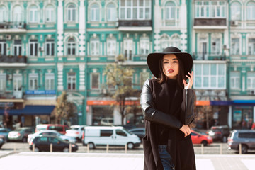 Fashionable young model in hat posing at the background of city street