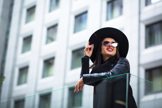 Happy brunette woman wears glasses and hat at the street. City lifestyle
