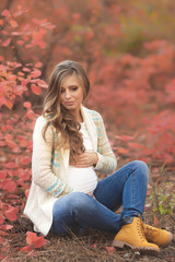 Obraz premium Portrait of young pregnant woman in casual clothes walking in red autumn park