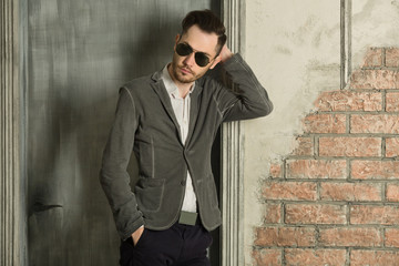 young handsome man with unshaven on his face wearing black glasses with a pensive look in a suit against the background of a light wall