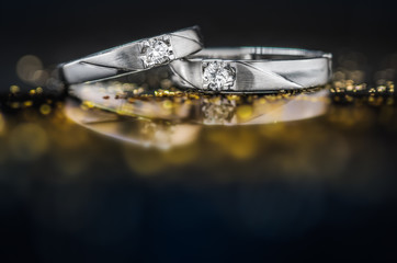 Close up pair of Platinum wedding rings with diamond on bokeh reflection background