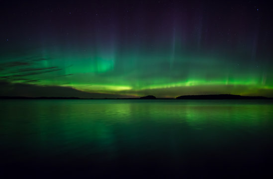 Northern lights dancing over calm lake. Farnebofjarden national park in Sweden.