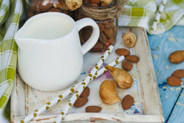 Obraz na płótnie Canvas Almonds in the glass, jar with milk on the wooden tray and decorative tubes for drink