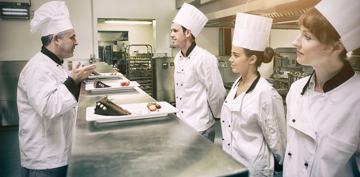 Chefs presenting their dessert plates to head chef in kitchen