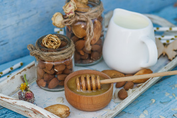 Honey in the wooden bowl, almonds and jar with milk on the wooden tray