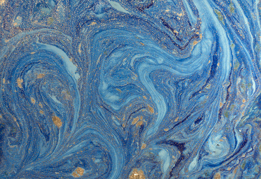 Marbled blue abstract background with golden sequins. Liquid marble ink pattern.