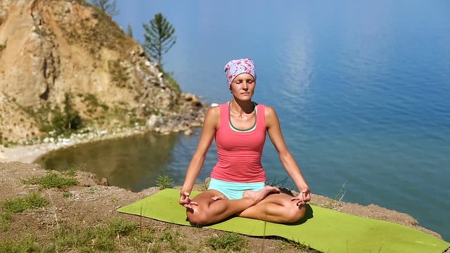 Young brunette professional yoga woman practices yoga moves outdoors. Girl is meditating. blue lake baikal on the background