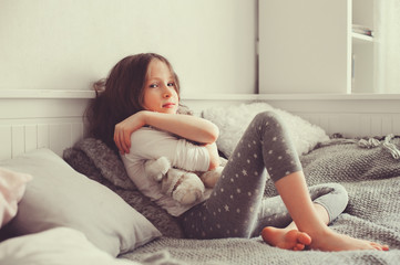 happy kid girl playing with teddy bears in her room, sitting on bed in pajama