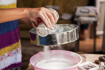 Hands sifting flour from glass through sieve in a bowl on a table